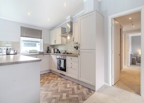 A modern kitchen with white cabinetry, a herringbone wood floor, and a visible oven.