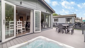 Una terraza con jacuzzi, mobiliario exterior y un ventanal corredero que da a una habitación.