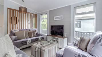 Una sala de estar moderna con sofá, reposapiés y televisor, listones de madera en la pared y ventanas amplias.