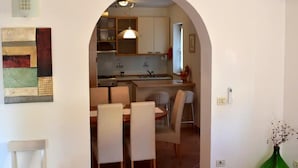 Un área de comedor con una mesa y sillas, una cocina al fondo y una botella verde en el suelo.