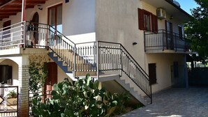 Una casa de dos pisos con una escalera que lleva a un balcón, un jardín pequeño y una chimenea.