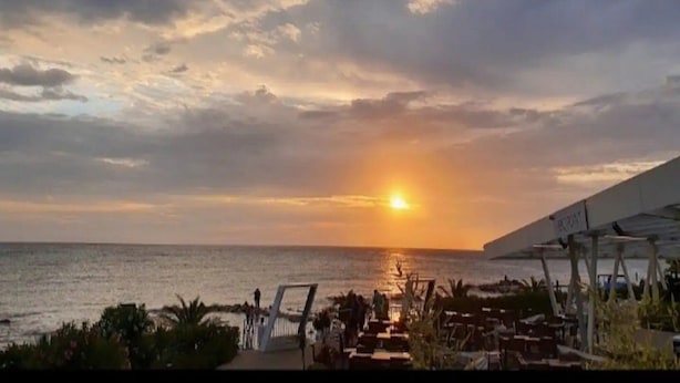Vista del atardecer desde un lugar frente a la playa, con un sendero que lleva al agua y vista al océano.