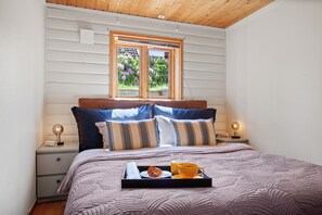 A neatly made bed with a tray of breakfast items, a bedside lamp, and a window with a view of flowers. - Krokenskogen (Sandefjord)