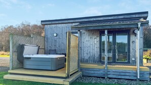 A modern wooden cabin with a hot tub, a deck, and a glass door leading to a covered patio. - This Studio Lodge is perfect for couples. (Ringford)