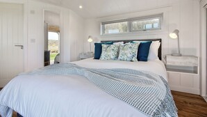 A bedroom with a large bed, two bedside tables, a window, and a door. - This Studio Lodge is perfect for couples. (Ringford)