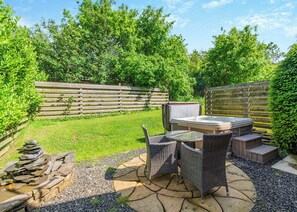 A patio with a hot tub, wicker furniture, and a stone fire pit.