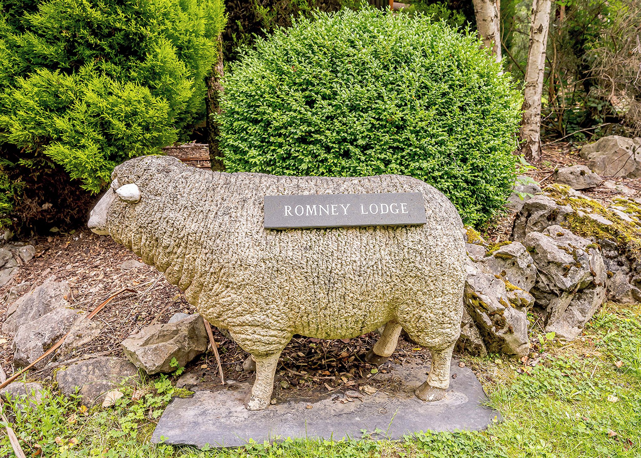 Una escultura de piedra de un carnero con una placa que dice 'ROMNEY LODGE' en un jardín.
