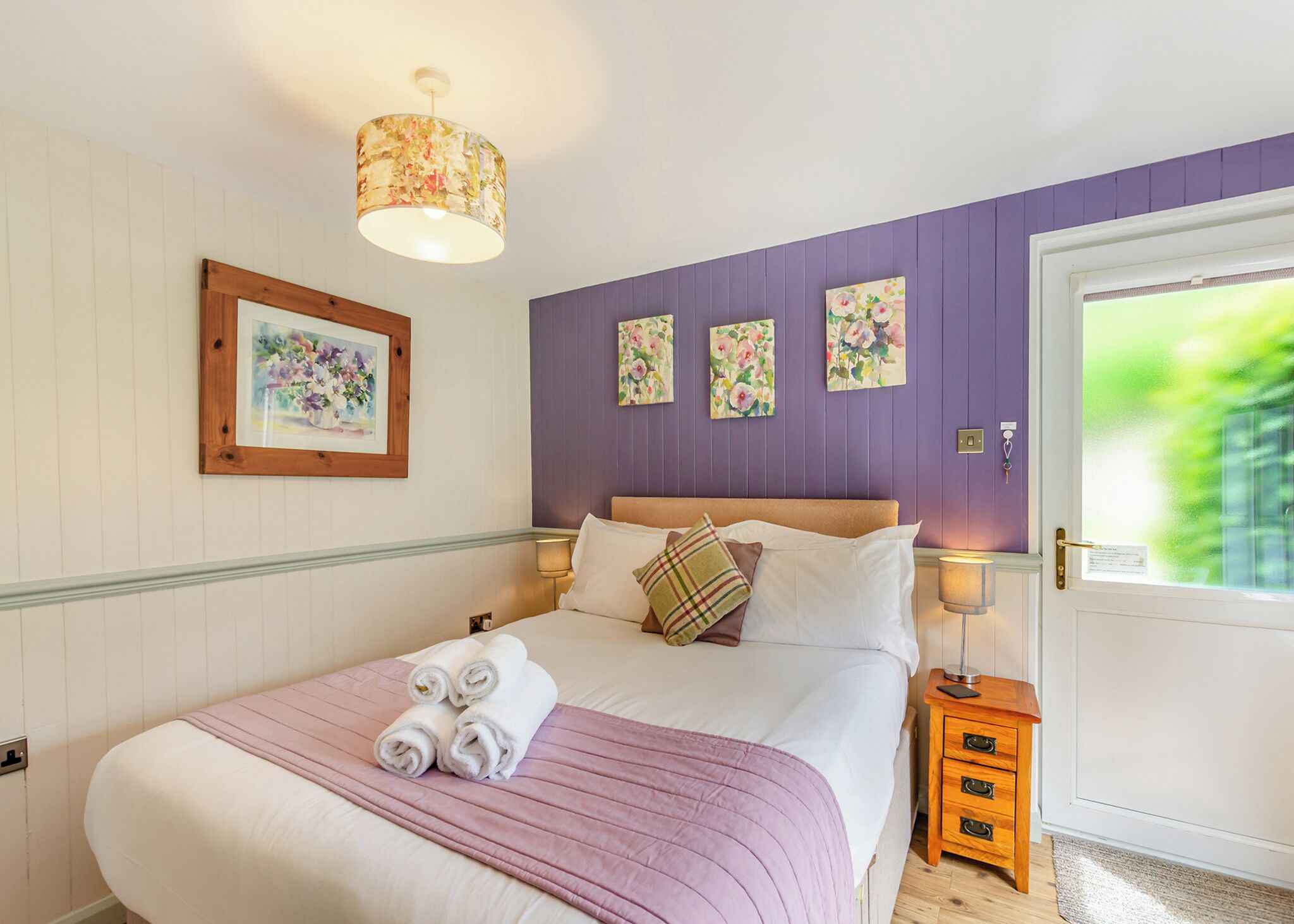 A bedroom with a bed, a bedside table, a lamp, and a door with a view.