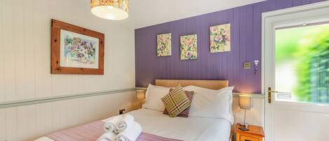 A bedroom with a bed, a bedside table, a lamp, and a door with a view.