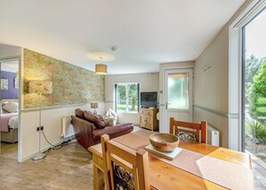 A cozy living room with a sofa, a dining table with a bowl, a television, and a window with a view of greenery.