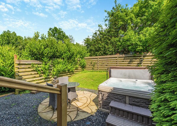 A backyard with a hot tub, a wooden deck, and a stone patio.