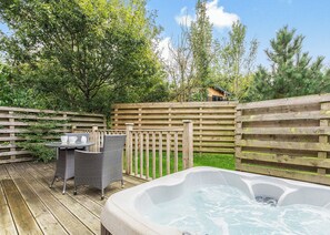 A wooden deck with a hot tub, wicker chairs, and a table with cups.