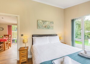 A bedroom with a bed, bedside lamps, a painting, a window with a view, and a door leading to a dining area.
