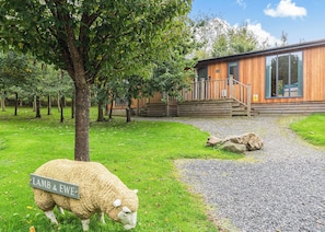 Ein Holzhaus mit Kiesweg, einem Schaf und einem Schild mit der Aufschrift 'LAMB & EWE'.