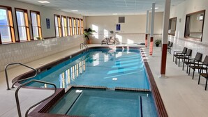 Ein großes Hallenbad mit deutlich abgegrenzten Bahnen, einem Rettungsschwimmerstuhl und einem Sitzbereich mit Stühlen.