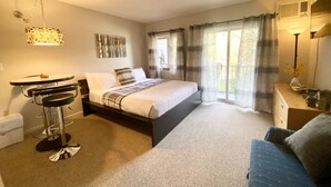 Ein Hotelzimmer mit Bett, Schreibtisch, Stuhl, Sofa und einem Balkon mit Vorhängen.