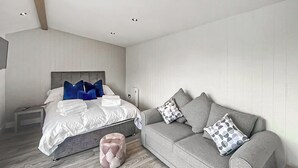 Une chambre à coucher moderne avec un lit, un canapé gris et un petit pouf.