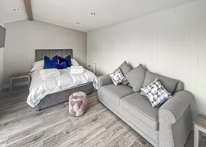 A modern bedroom with a bed, a grey sofa, and a small ottoman.