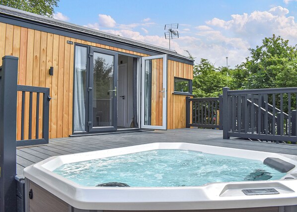A wooden building with glass doors, a hot tub, and a deck.