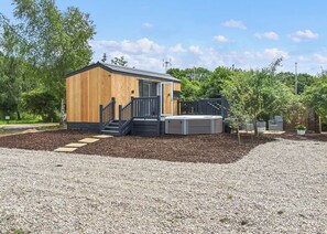 A wooden cabin with a deck, a hot tub, and a small garden area.