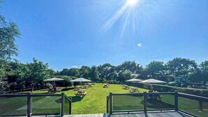 Un espace extérieur ensoleillé, aménagé avec des tables de pique-nique et des parasols, et entouré d’arbres.