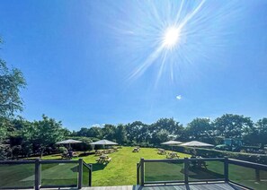 Ein sonniger Außenbereich mit Picknicktischen und Sonnenschirmen, umgeben von Bäumen.