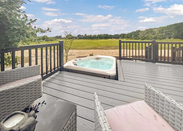 A hot tub on a wooden deck with a view of a grassy field.