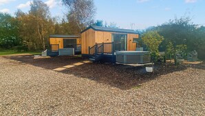 Eine kleine Holzhütte mit Veranda und Whirlpool, umgeben von Kies und Bäumen.