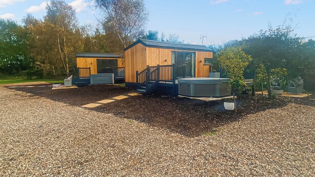 Une petite cabane en bois dotée d’une véranda et d’un jacuzzi, entourée de gravier et d’arbres.