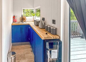 A narrow kitchen with blue cabinets, a wooden countertop, and a window with a view of greenery.