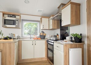 A compact kitchen with a microwave, stove, oven, and a window with blinds.