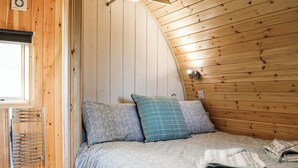 A bedroom with a sloped ceiling, wooden walls, a bed with patterned bedding, a window, and a wall-mounted light fixture. - 1 bedroom accommodation in Troutbeck (Troutbeck)