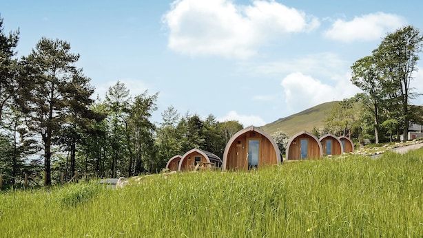 A row of wooden dome-shaped cabins with doors, set in a grassy field with trees and a hill in the background. - 1 bedroom accommodation in Troutbeck (Troutbeck)