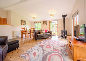 A living room with a sofa, a TV, a fireplace, a dining area with chairs, and a view through the door.