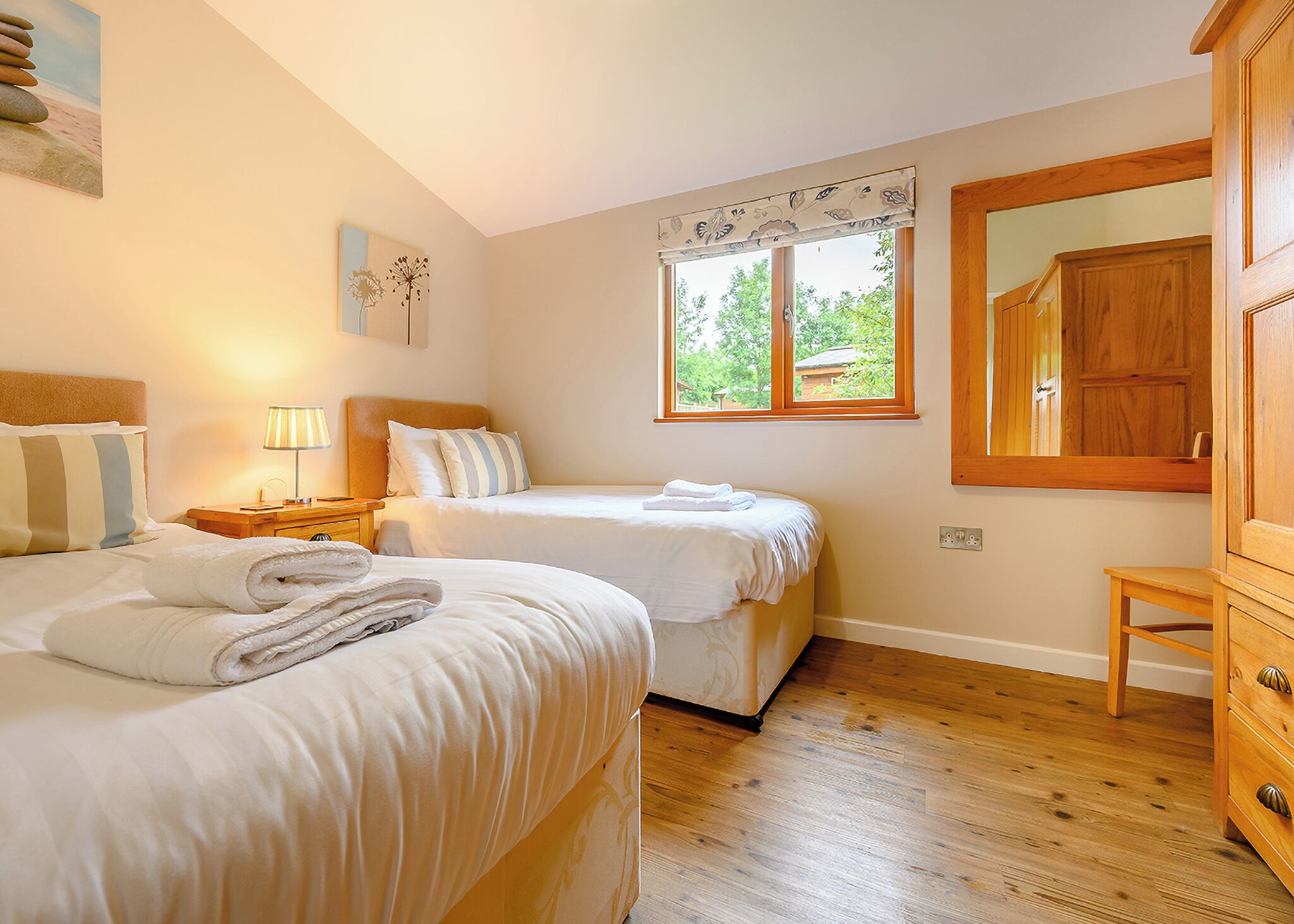 A bedroom with two beds, a nightstand, a lamp, a window with a view, and a wooden cabinet.