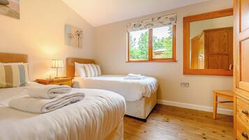 A bedroom with two beds, a nightstand, a lamp, a window with a view, and a wooden cabinet.