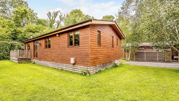 A wooden cabin with a deck, surrounded by a well-maintained lawn and trees.