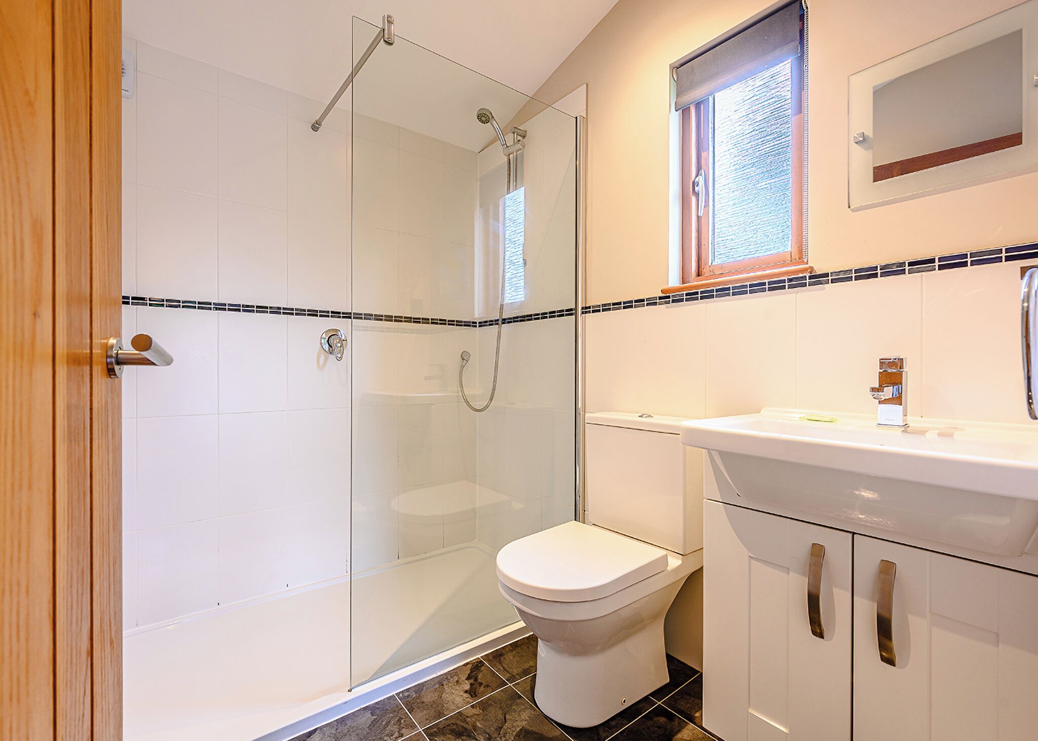 A bathroom with a glass-enclosed shower, a toilet, and a sink with a mirror above it.