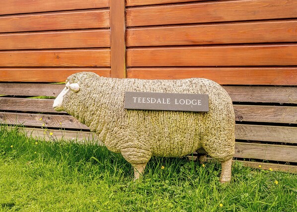 A sheep sculpture with a plaque labeled 'TEESDALE LODGE' in front of a wooden wall.