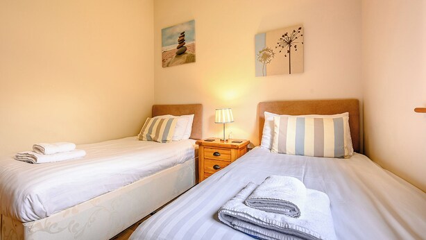 Quarto com duas camas de solteiro, mesa de cabeceira com abajur e quadros nas paredes.