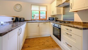 A modern kitchen with white cabinets, a granite countertop, a built-in microwave, a stove, and a clock on the wall. - Deluxe lodge with one master double with en suite walk-in shower and one twin. (Cartmel)