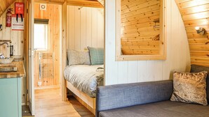 Interior de uma cabana de madeira com uma cama, um banco, um extintor de incêndio e uma janela.