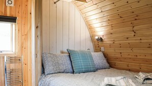 Um quarto em estilo loft com teto inclinado, paredes de madeira, cama embutida e janela com persiana rolo.