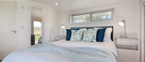 Ein Schlafzimmer mit einem Bett, zwei Nachttischen, einem Fenster und einer Tür.