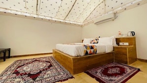 Un dormitorio con cama, mesita de noche, ventilador de techo y dos alfombras.