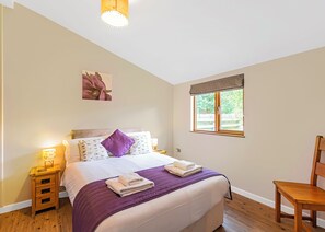 A bedroom with a bed, a nightstand, a chair, a window, and a painting on the wall.