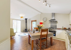 A spacious kitchen with a stove, oven, and a large chimney. There is a dining table with chairs and a vase of flowers.