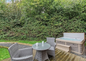 An outdoor patio with wicker furniture, a hot tub, and a dense green hedge in the background.