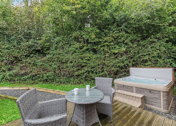 An outdoor patio with wicker furniture, a hot tub, and a dense green hedge in the background.
