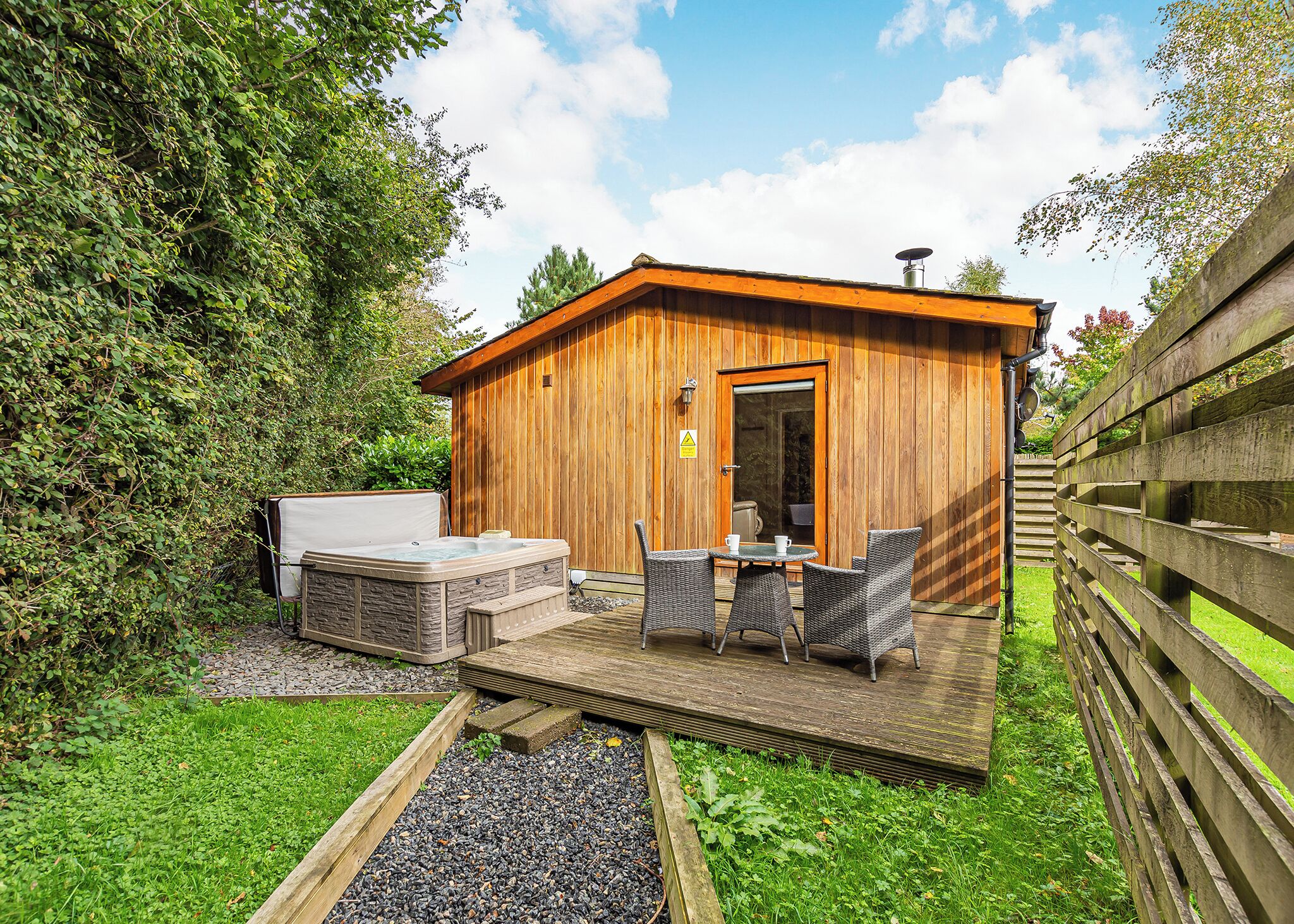 Een houten hutje met een jacuzzi, buitenzitplaatsen en een grindpad.